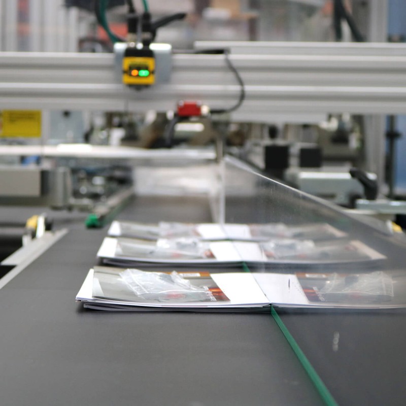 Printprodukte und Non-Print Artikel auf dem Förderband zur Beipackanlage, um in Folie eingeschweißt zu werden